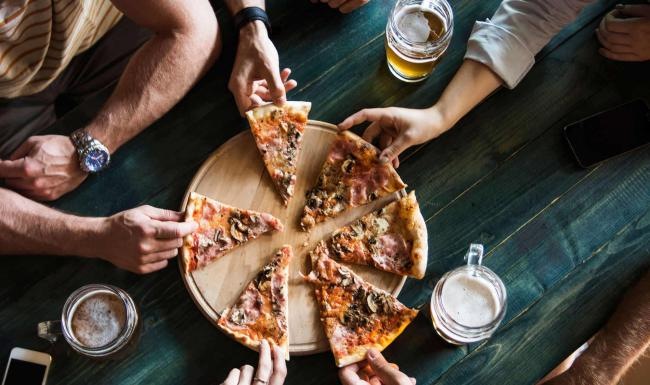 Vibrant community life with a variety of dining options A group of people sharing pizza at a table at The Hominy apartments in Candler, NC.